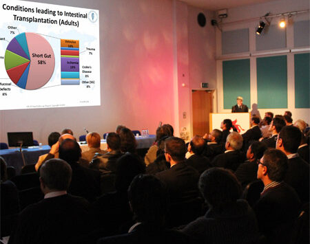 A packed audience watching a man giving a lecture.